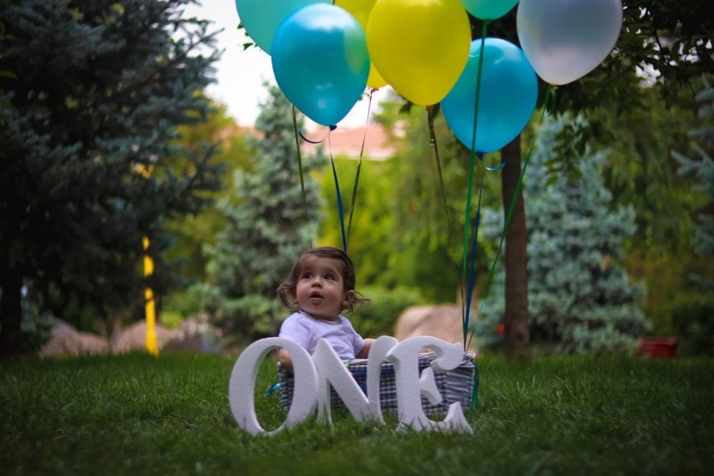 Adorable baby celebrating first birthday outdoors with colorful balloons.